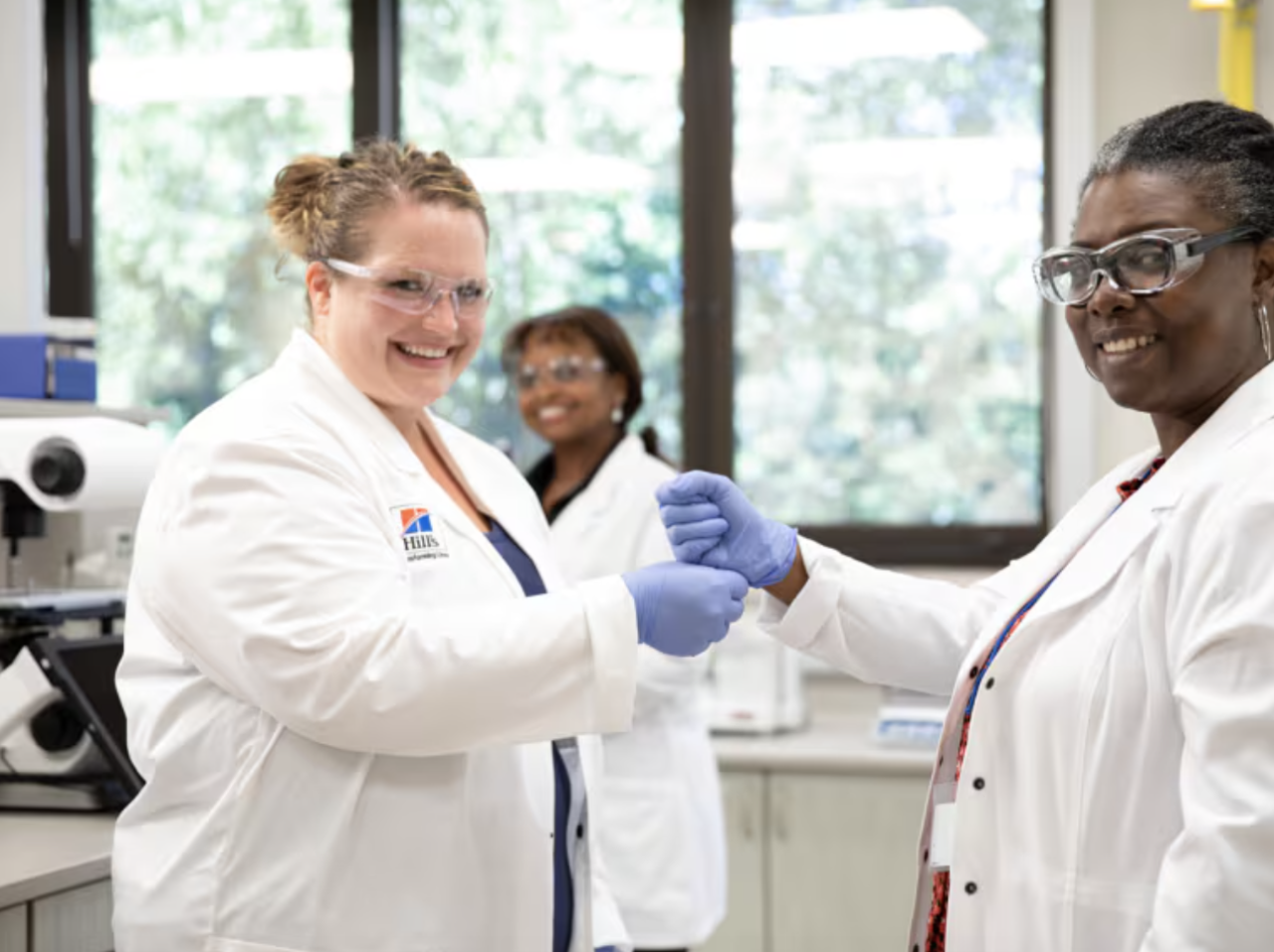 tres mujeres sonrientes, científicas con batas blancas y gafas protectoras